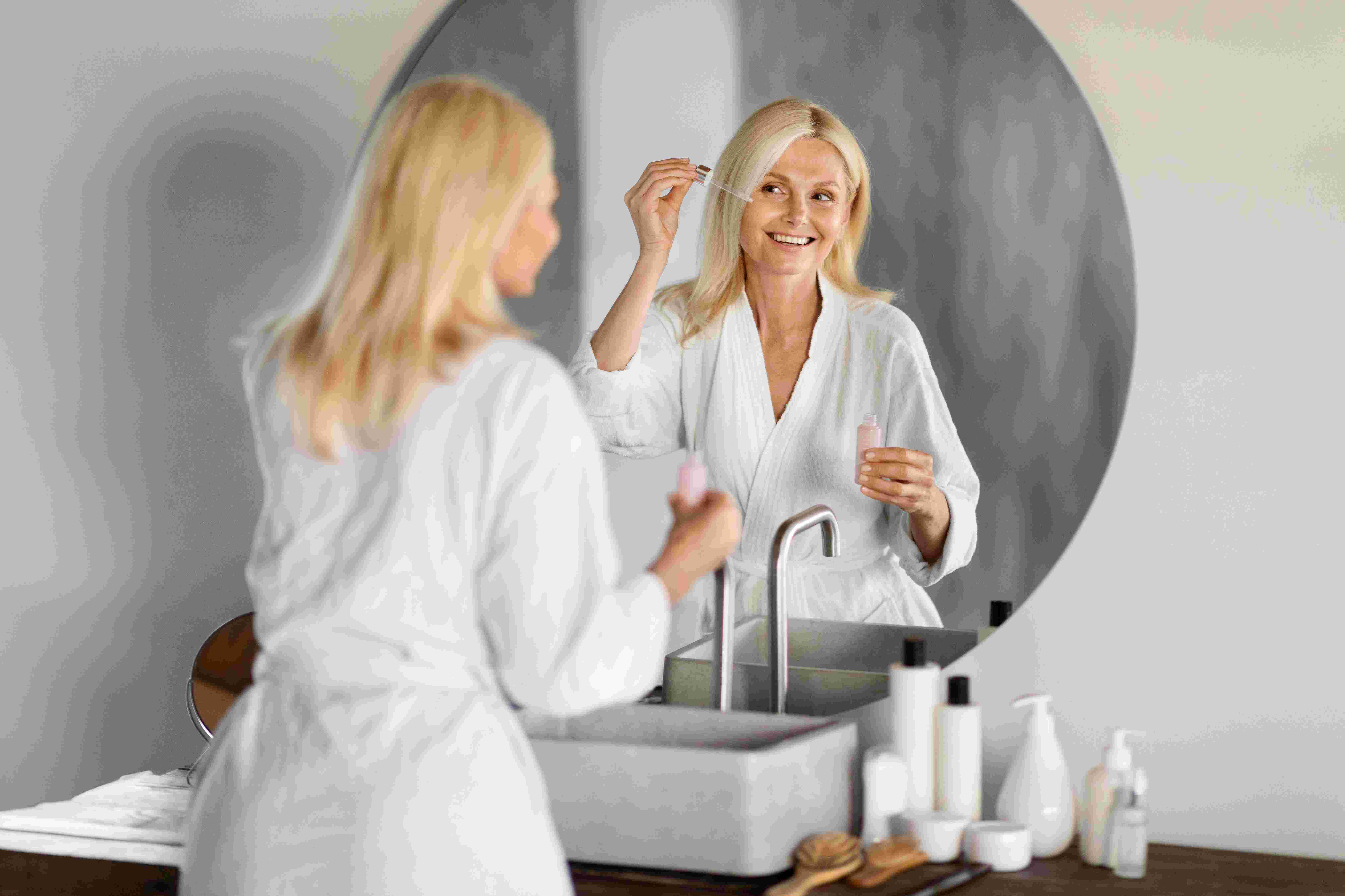 Mature woman looking in mirror, applying skincare products.